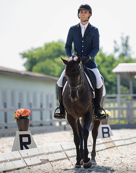 Fid'Equin : Photo avec au centre d'une carrière d'entrainement de sable, un cavalier professionnel avec son cheval. Pot de fleur à gauche. Lumière naturelle.